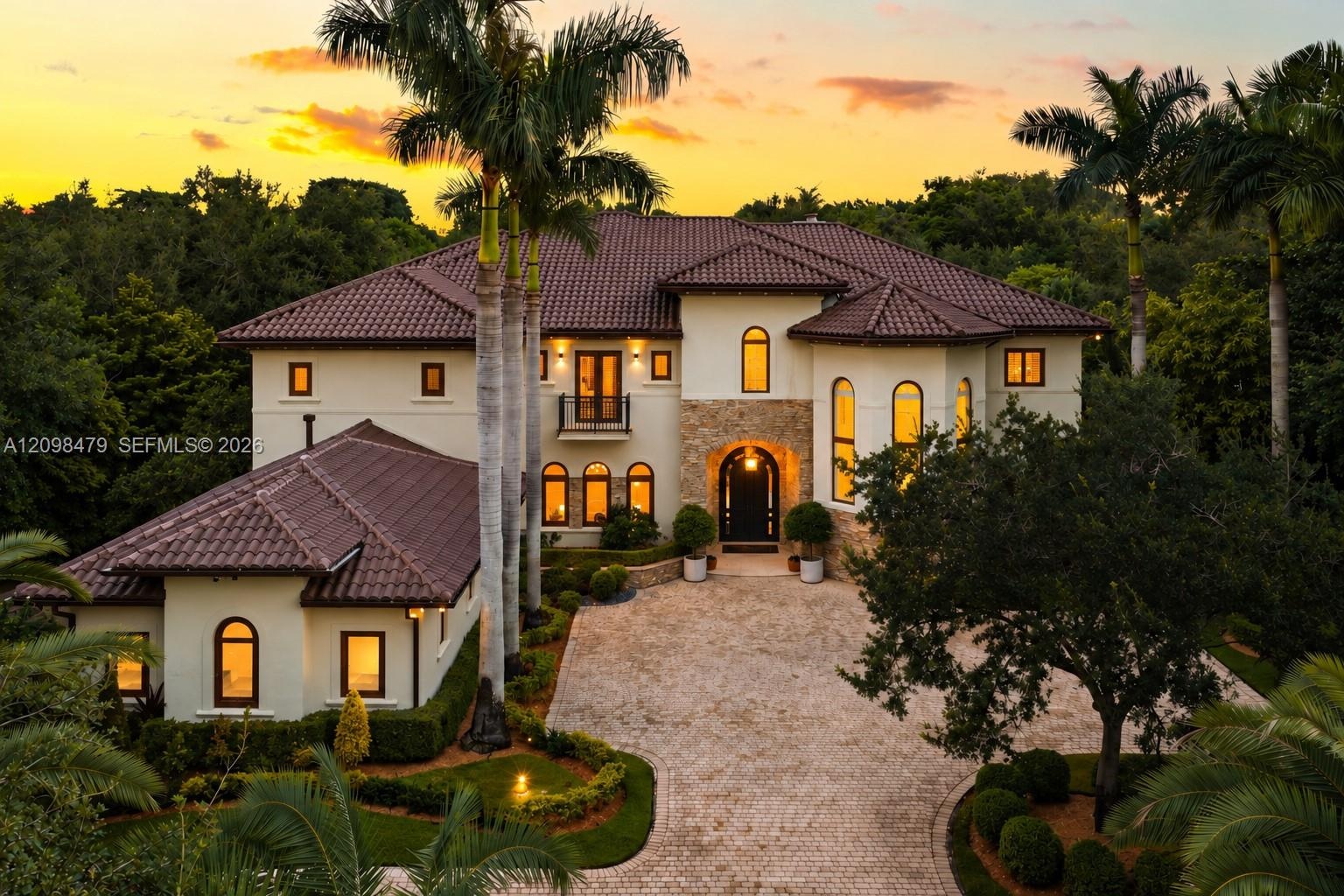 Stucco exterior featuring a tile roof, stone masonry accents, arched window detailing, and a paved motor court