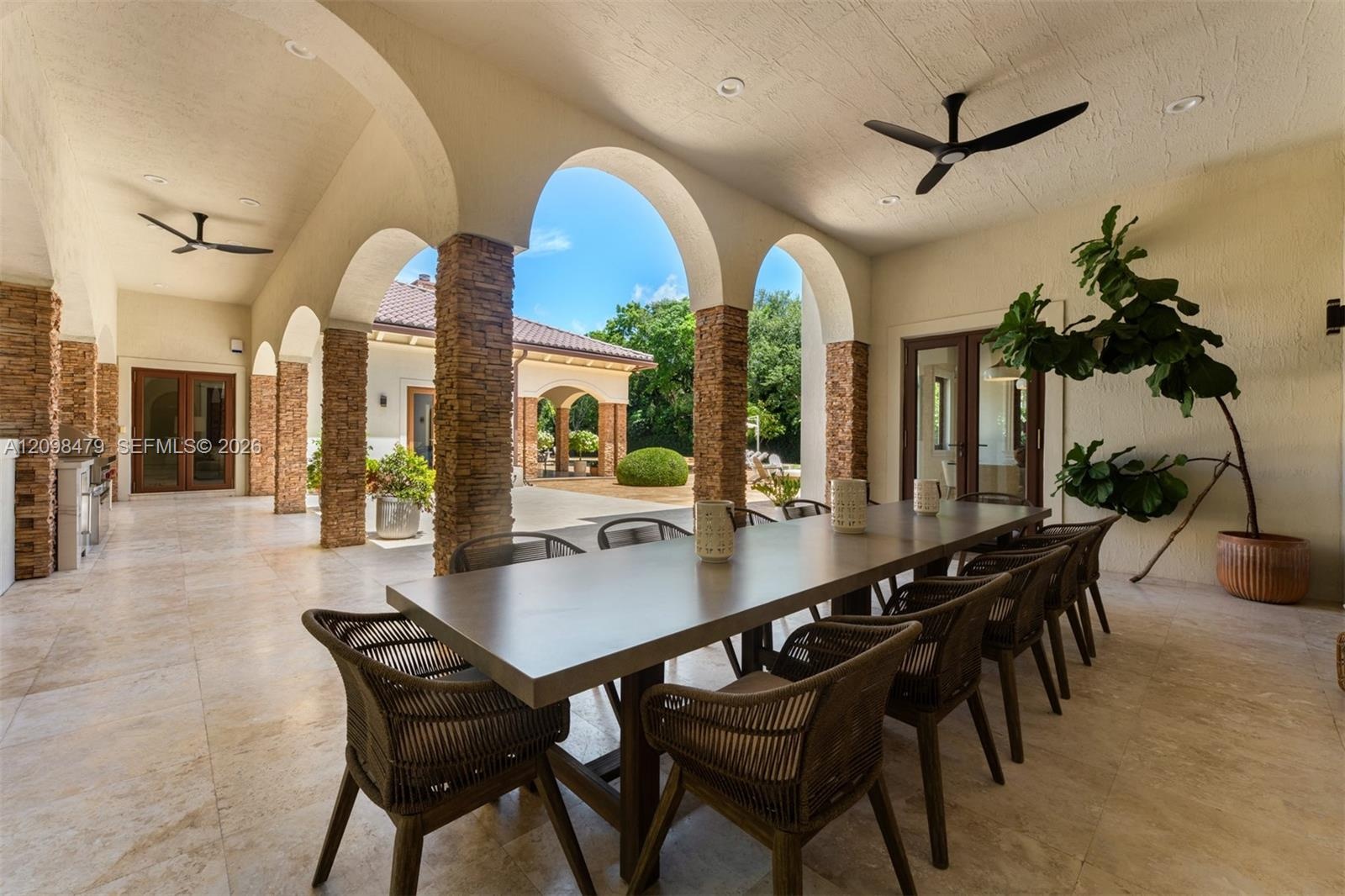Covered patio featuring arched walkways, stone-clad columns, tile flooring, and integrated ceiling fans