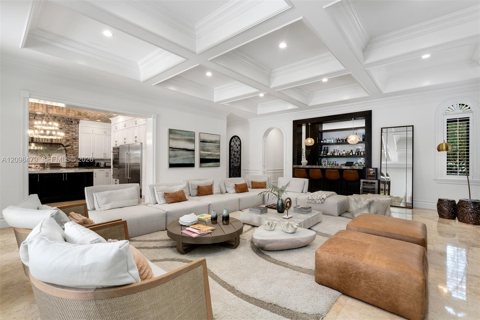 Coffered ceiling with recessed lighting, integrated wet bar, arched doorway, arched window with plantation shutters, and polished stone flooring