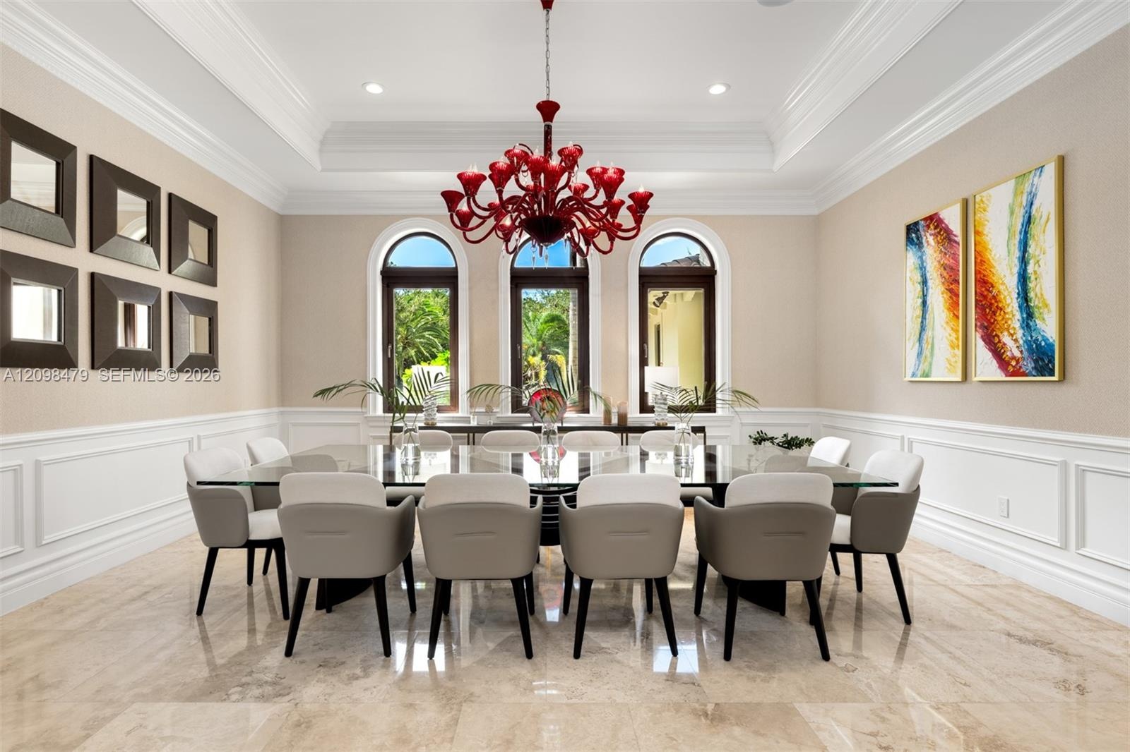 Recessed ceiling with layered crown molding, arched windows, wainscoting, and large format tile flooring