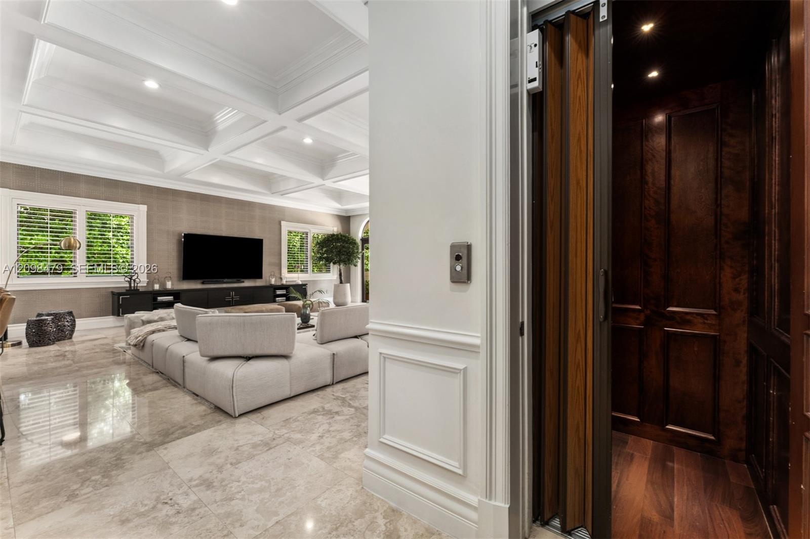 Polished stone flooring, coffered ceiling, multiple windows with plantation shutters, wood-paneled interior elevator, and recessed lighting