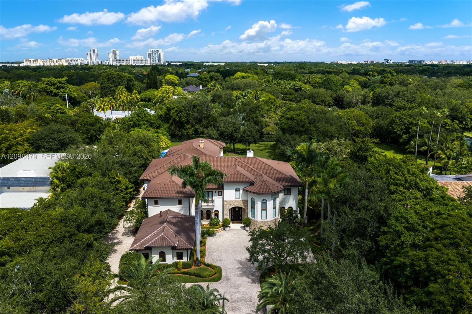 Expansive property featuring a Mediterranean-inspired residence with a tile roof, a circular driveway, and lush surrounding trees