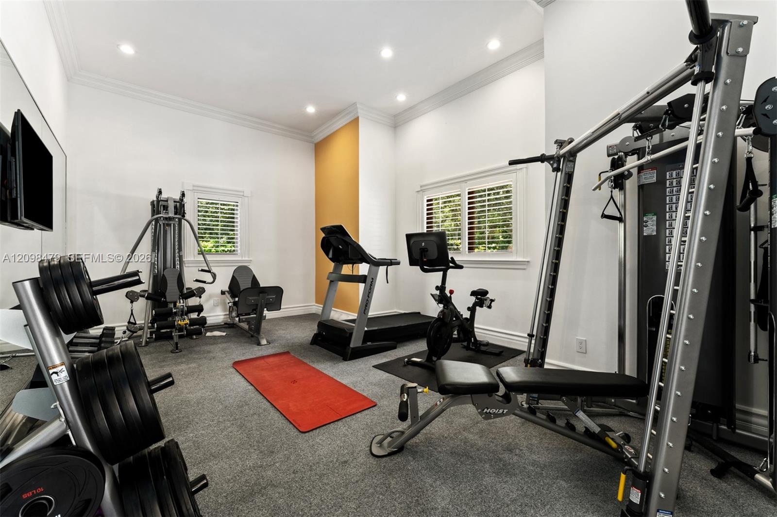 Dedicated fitness space featuring recessed lighting, crown molding, and two windows with plantation shutters