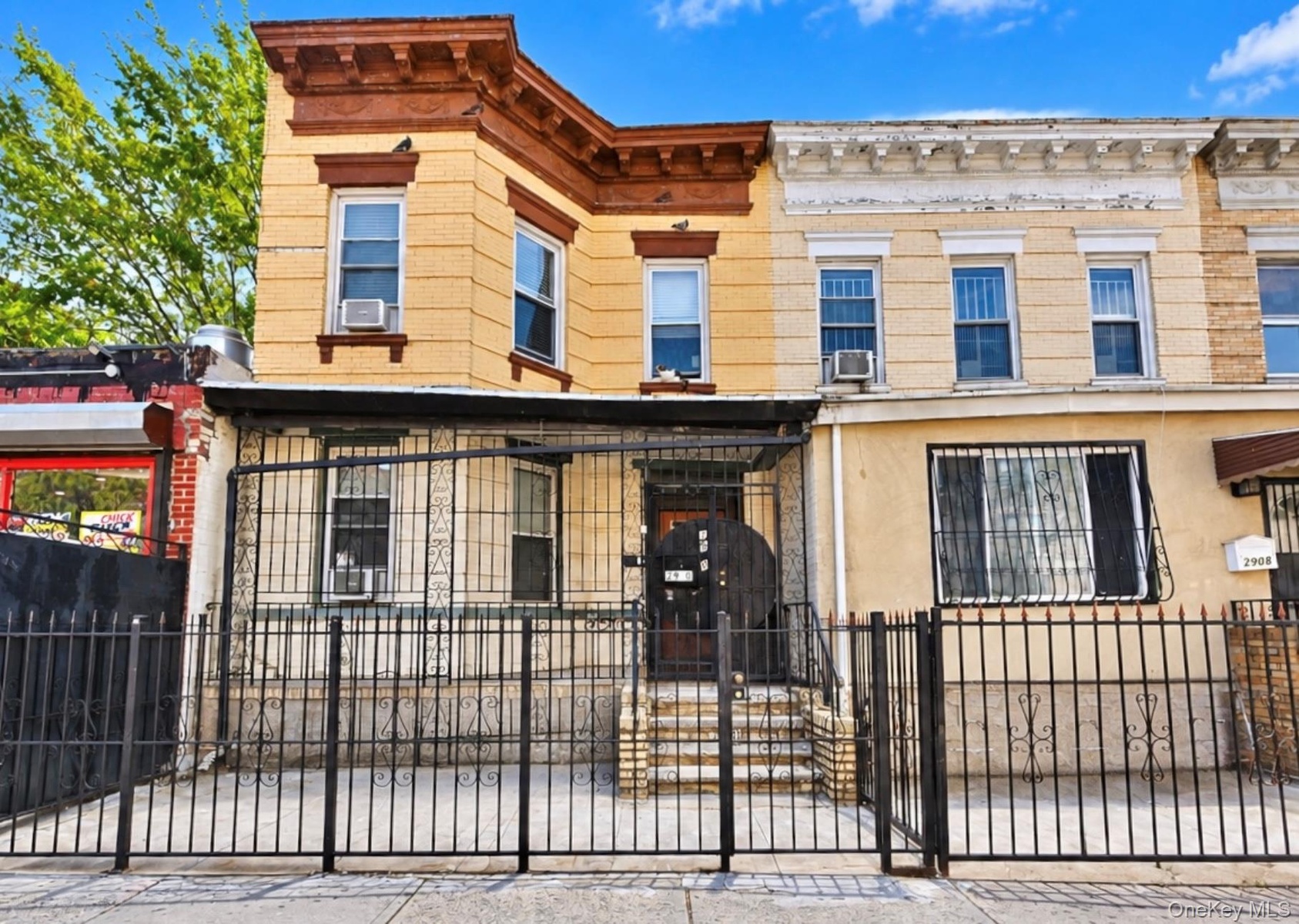 Multi-story masonry facade featuring detailed cornice work, a structural bay, metal window security bars, and a metal perimeter fence