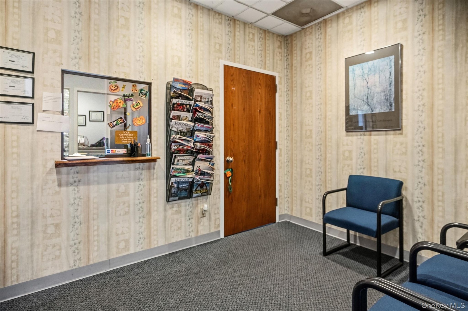 Interior space featuring neutral wallpaper, a solid wood-finish door, a pass-through window with a wood-finish ledge, and carpeted flooring