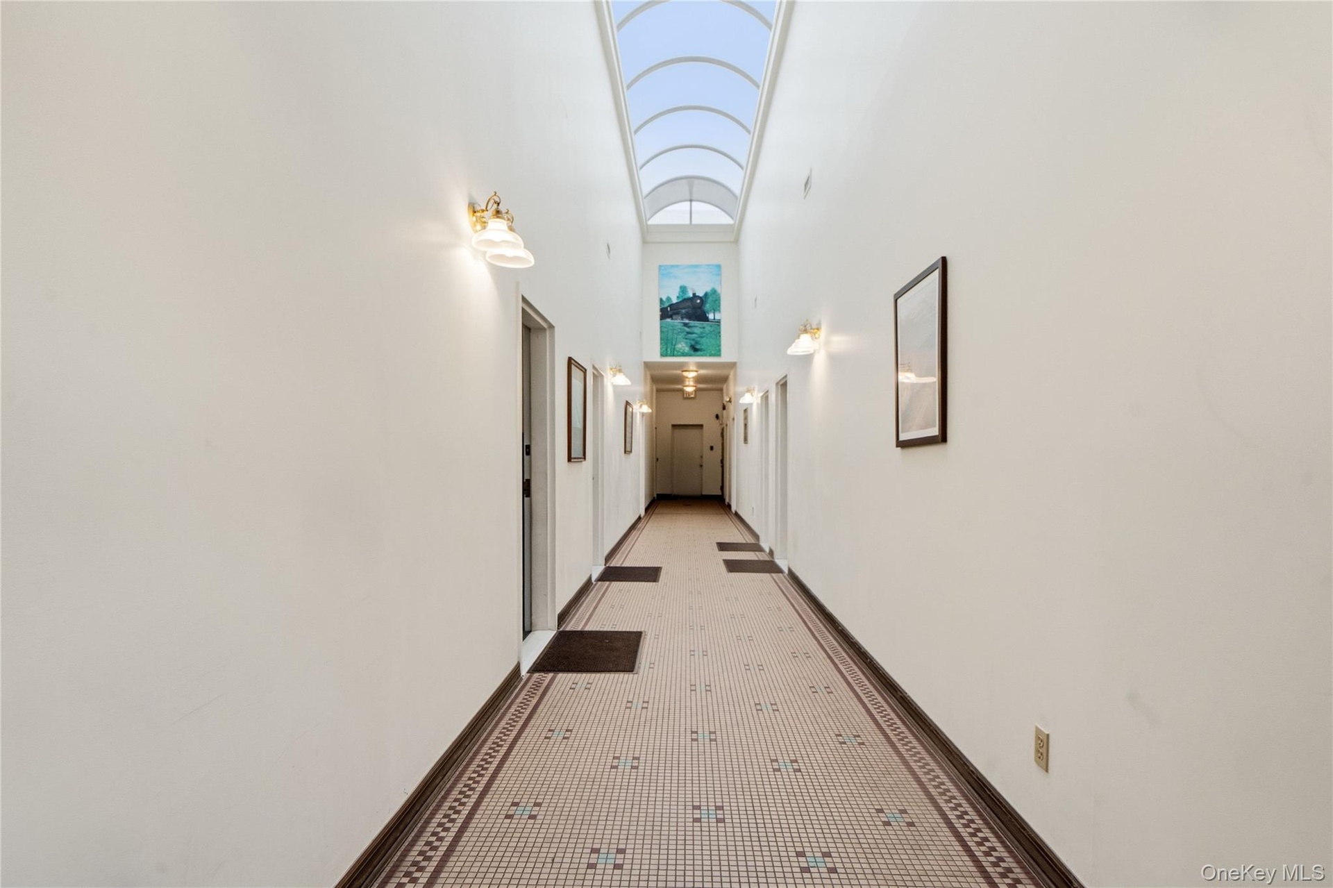 Hallway featuring an arched vaulted skylight, patterned tile flooring, and wall-mounted sconce lighting