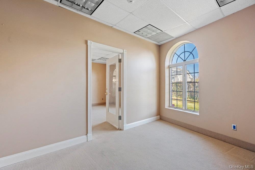 Arched window with decorative muntins, carpeted flooring, drop ceiling with recessed lighting, and a single-light glass-panel interior door