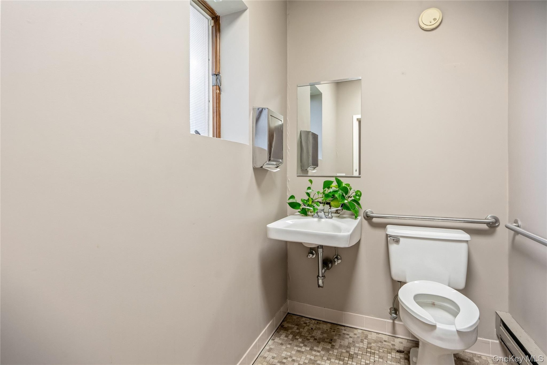 Wall-mounted sink with a rectangular basin, metallic wall-mounted paper dispenser, framed mirror, and chrome grab bars