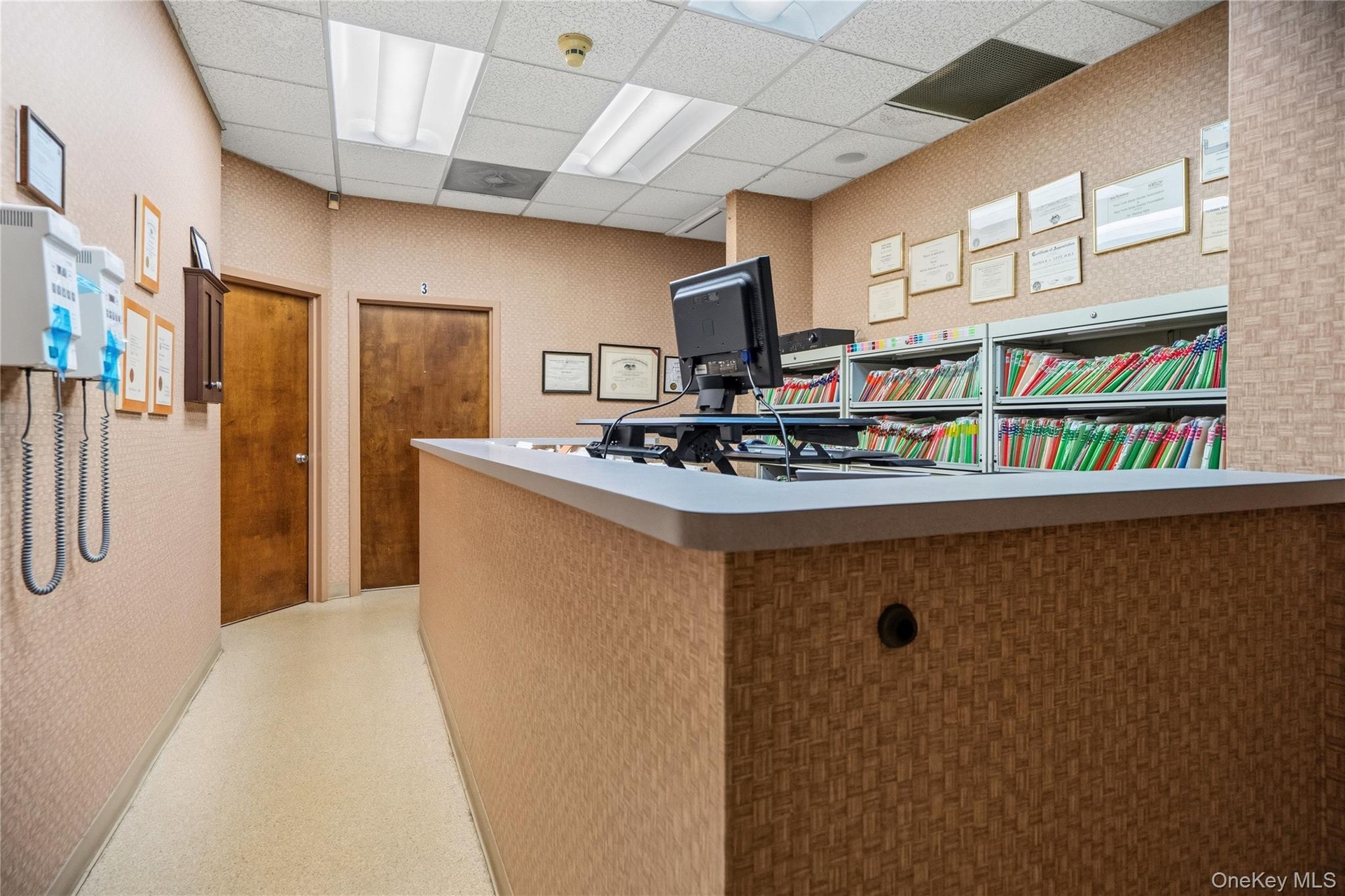 Reception area featuring a built-in transaction counter with a durable surface, integrated metal shelving, wood-veneer doors, drop ceiling with recess