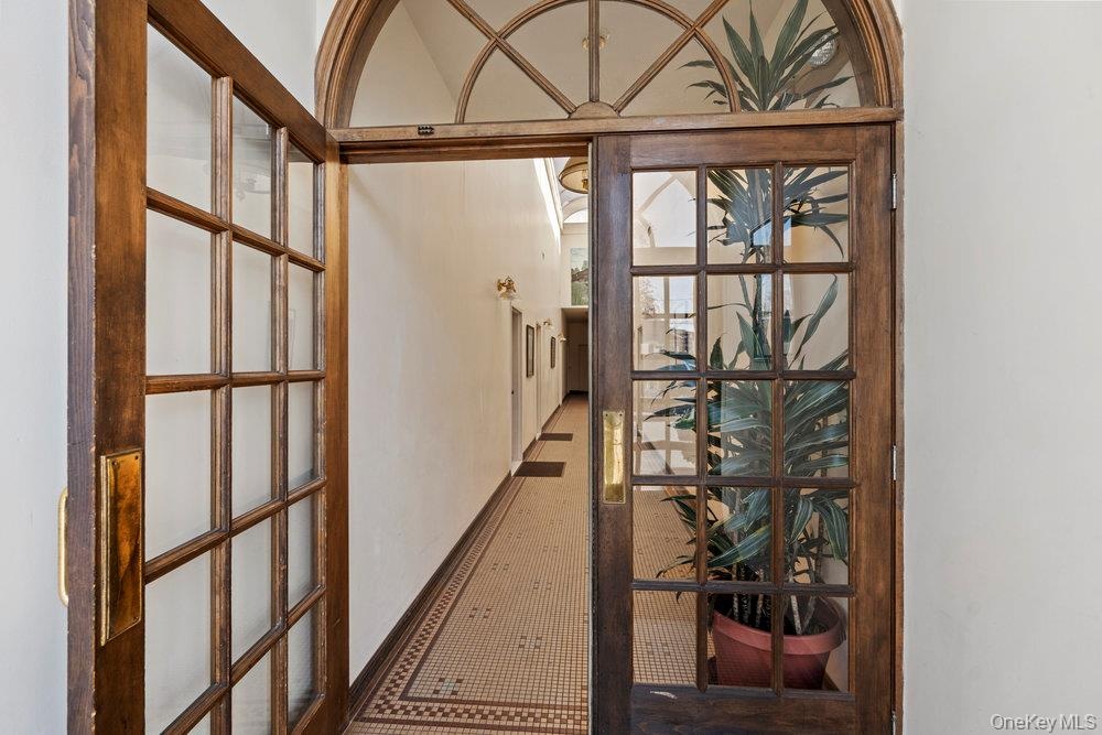 Double entry doors featuring a wooden frame, glass panes, and brass hardware, complemented by a semi-circular transom window and mosaic tile flooring