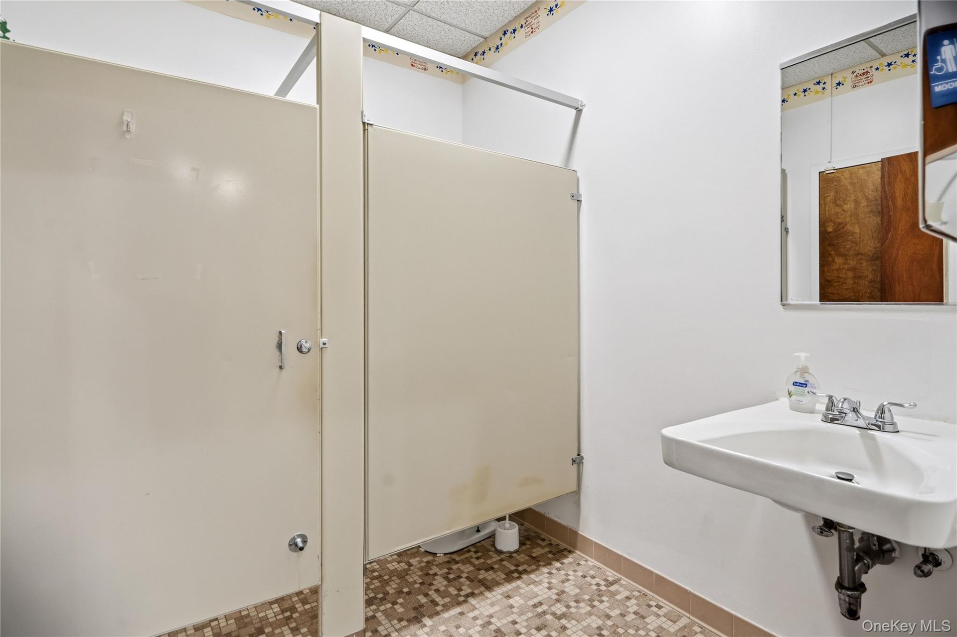 Restroom featuring floor-mounted partition stalls, a wall-mounted sink with chrome-finish hardware, and a framed wall mirror