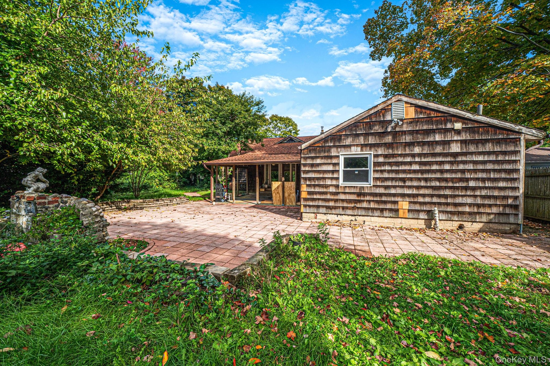Cedar shake siding, red paver patio, stone retaining wall, and covered porch area