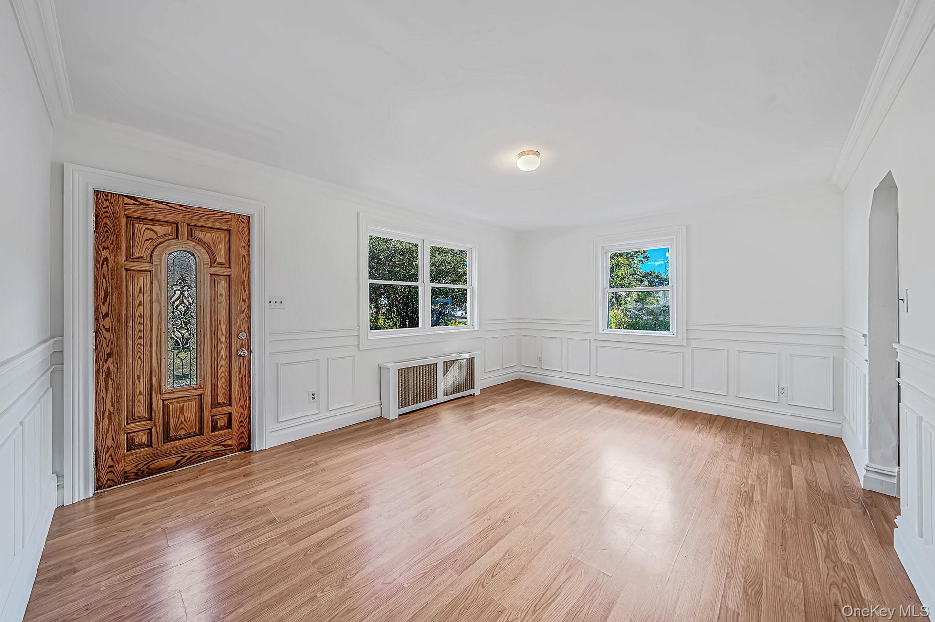 Solid wood front door with decorative glass inlay, laminate flooring, white wainscoting, and multi-pane windows