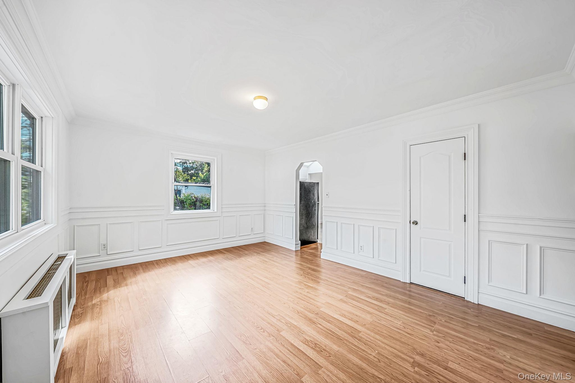 Bright freshly painted interior featuring laminated flooring, extensive wainscoting, crown molding, and arched doorway
