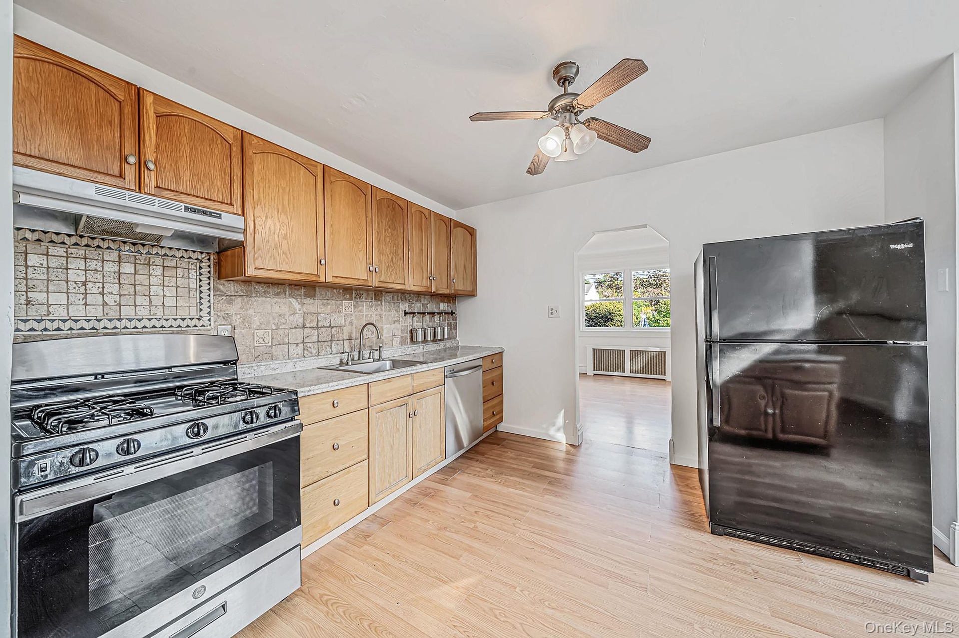 Kitchen featuring wood cabinetry, tile backsplash, stainless steel gas range and dishwasher.