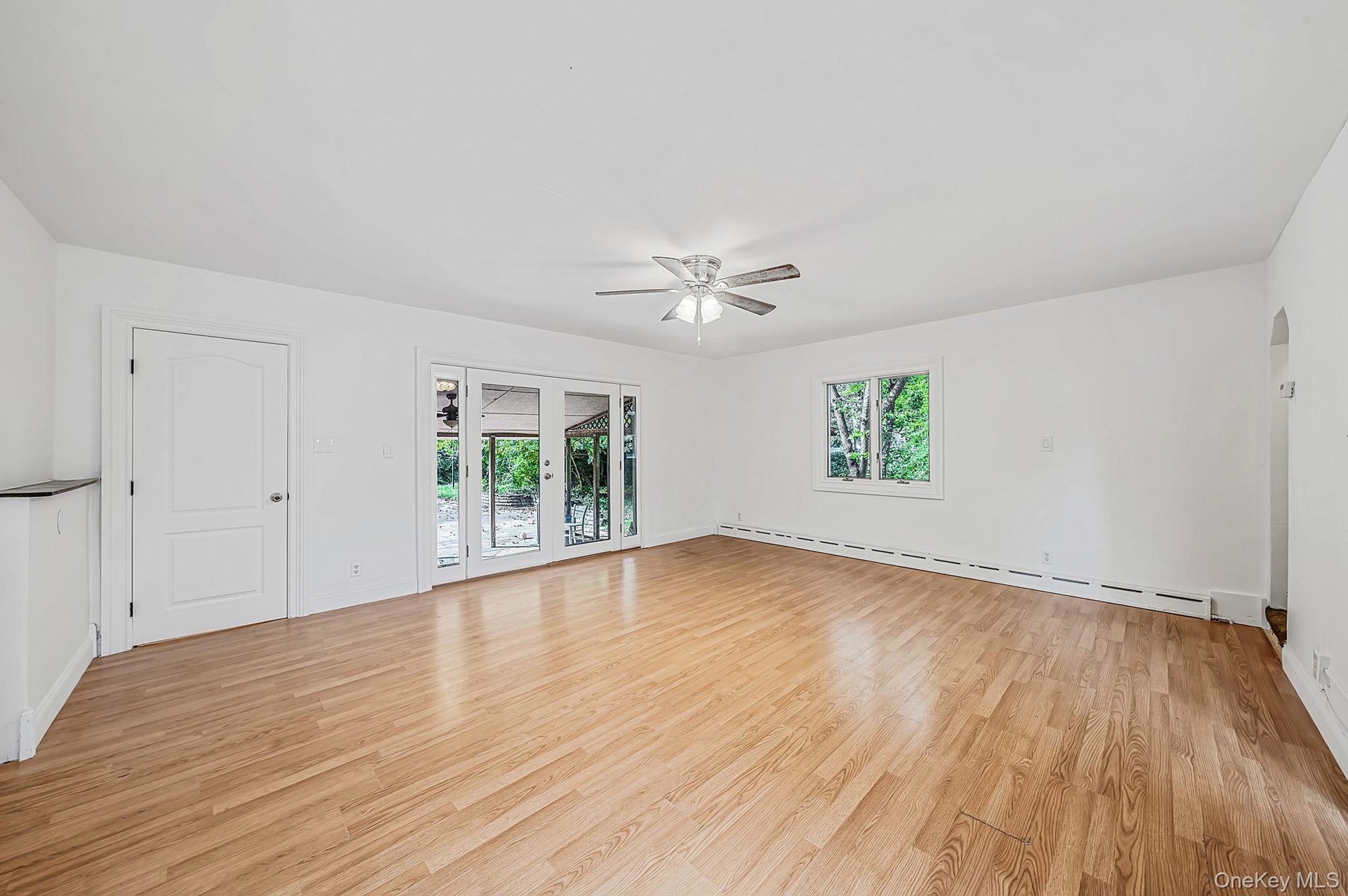 Spacious room featuring laminate flooring, a ceiling fan with integrated lighting, French doors that lead to covered patio and interior access to rear