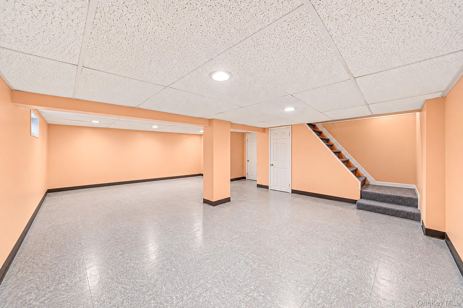 Partially finished lower level featuring a suspended acoustic tile ceiling, recessed lighting, neutral resilient flooring, and carpeted stairwell with