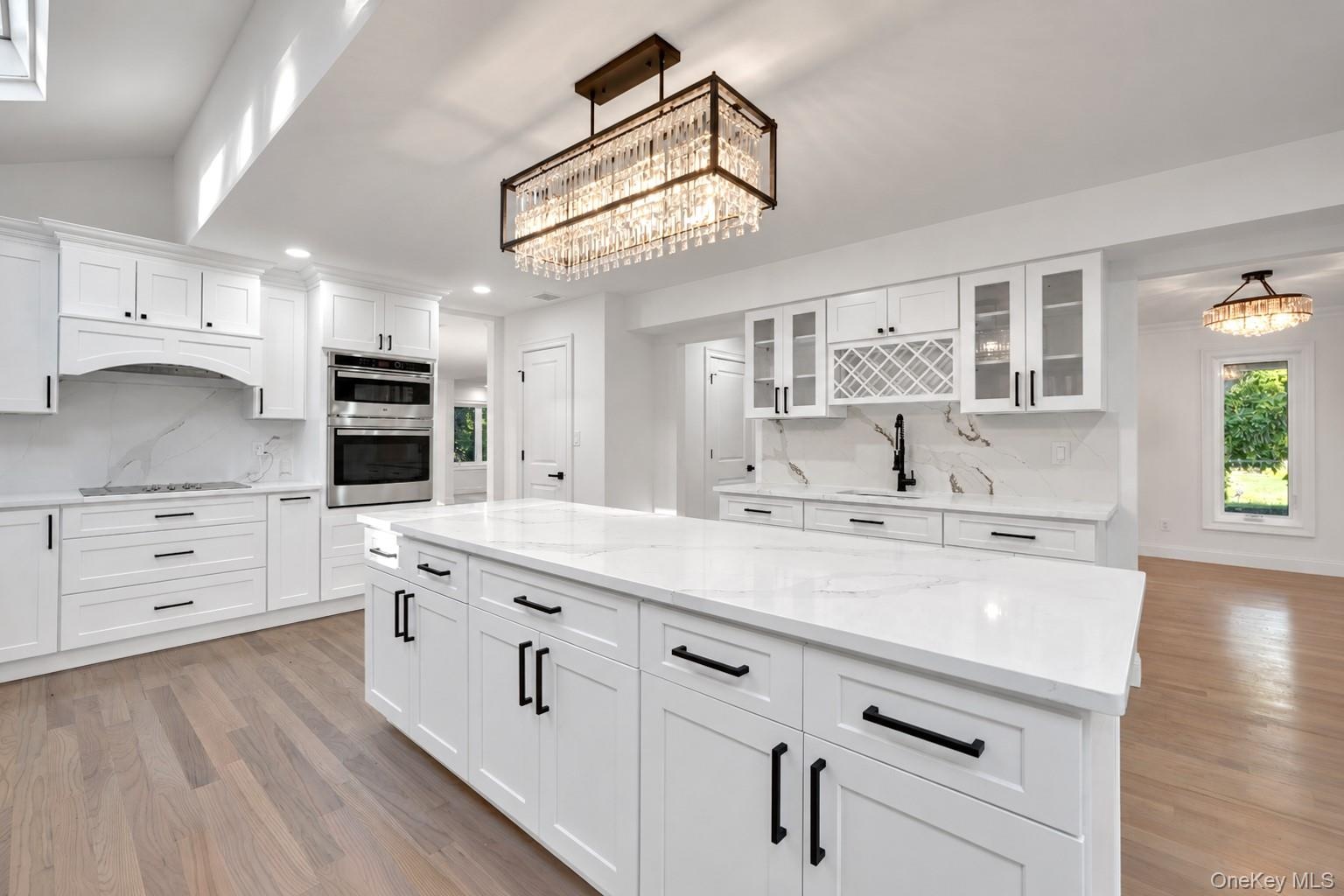 Kitchen featuring a large central island with light-toned stone surfacing, white cabinetry with matte black hardware, integrated wine rack, and a line