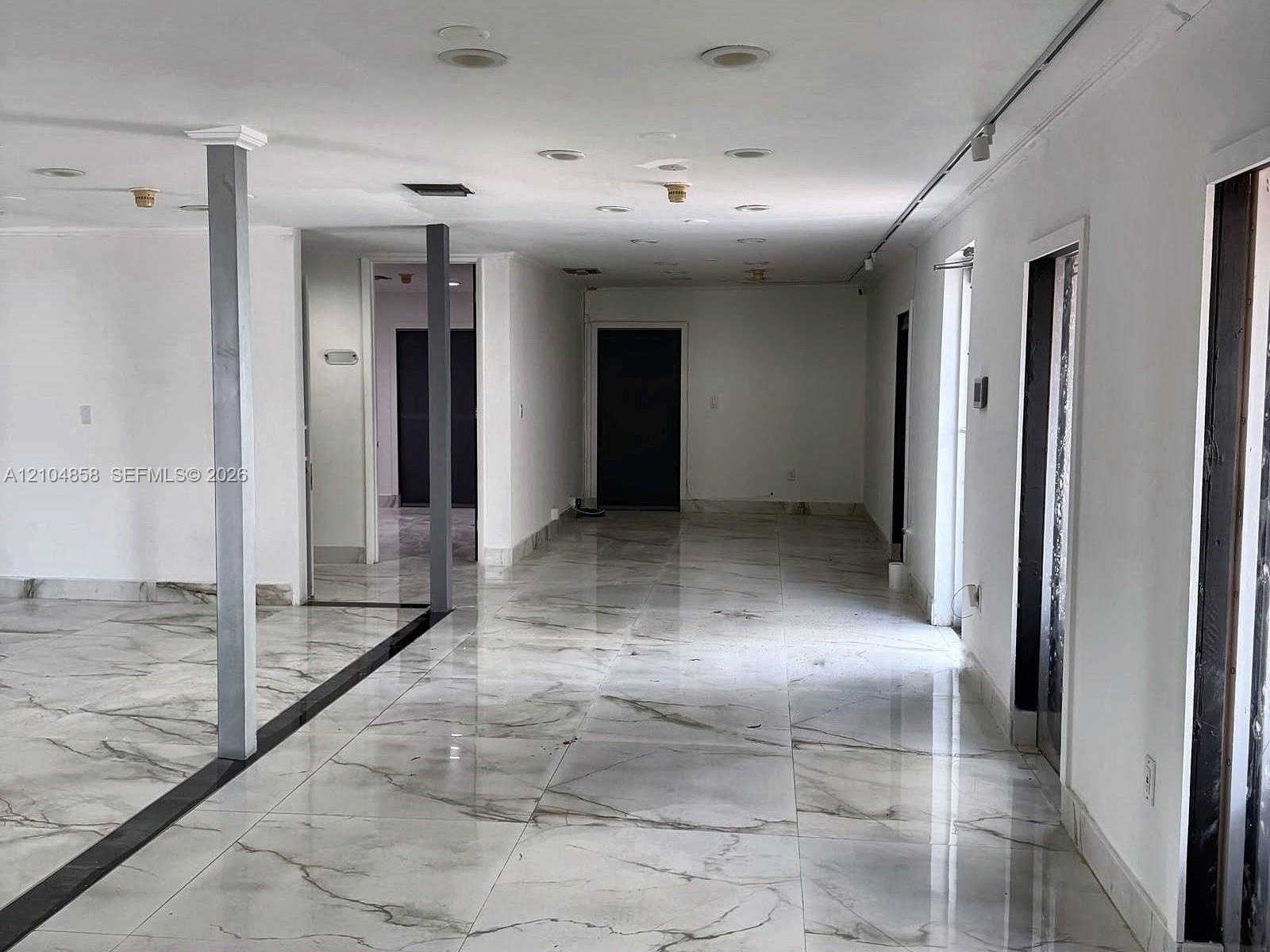Large-format stone-look tile flooring with grey veining, recessed ceiling lighting, and structural support columns