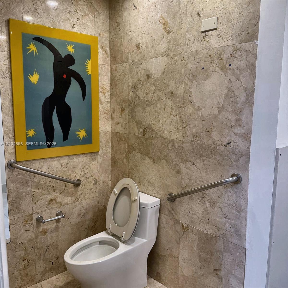 Full-height stone wall tiling, porcelain commode, and stainless steel grab bars