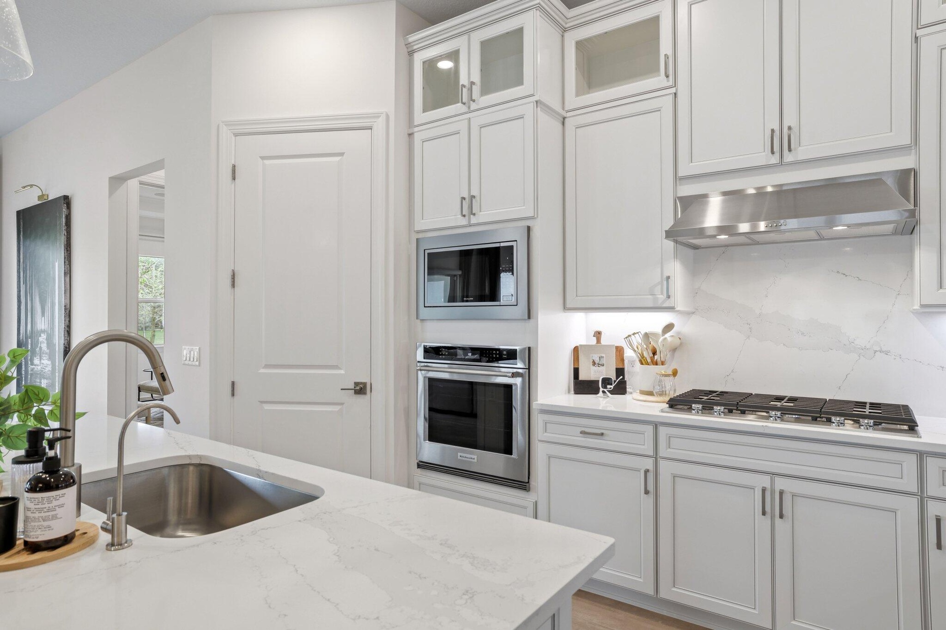 Kitchen featuring white cabinetry, quartz countertops with a full-height stone backsplash, stainless steel built-in double ovens, a gas cooktop, and a