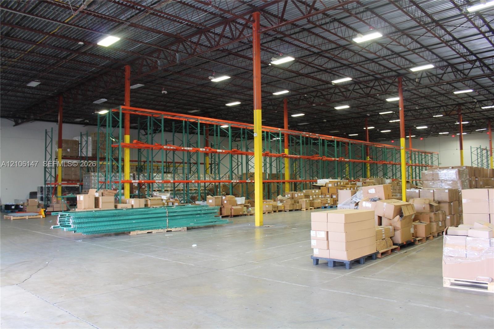 Warehouse interior featuring high-clearance open-span ceilings, steel truss construction, industrial lighting fixtures, concrete flooring, and install