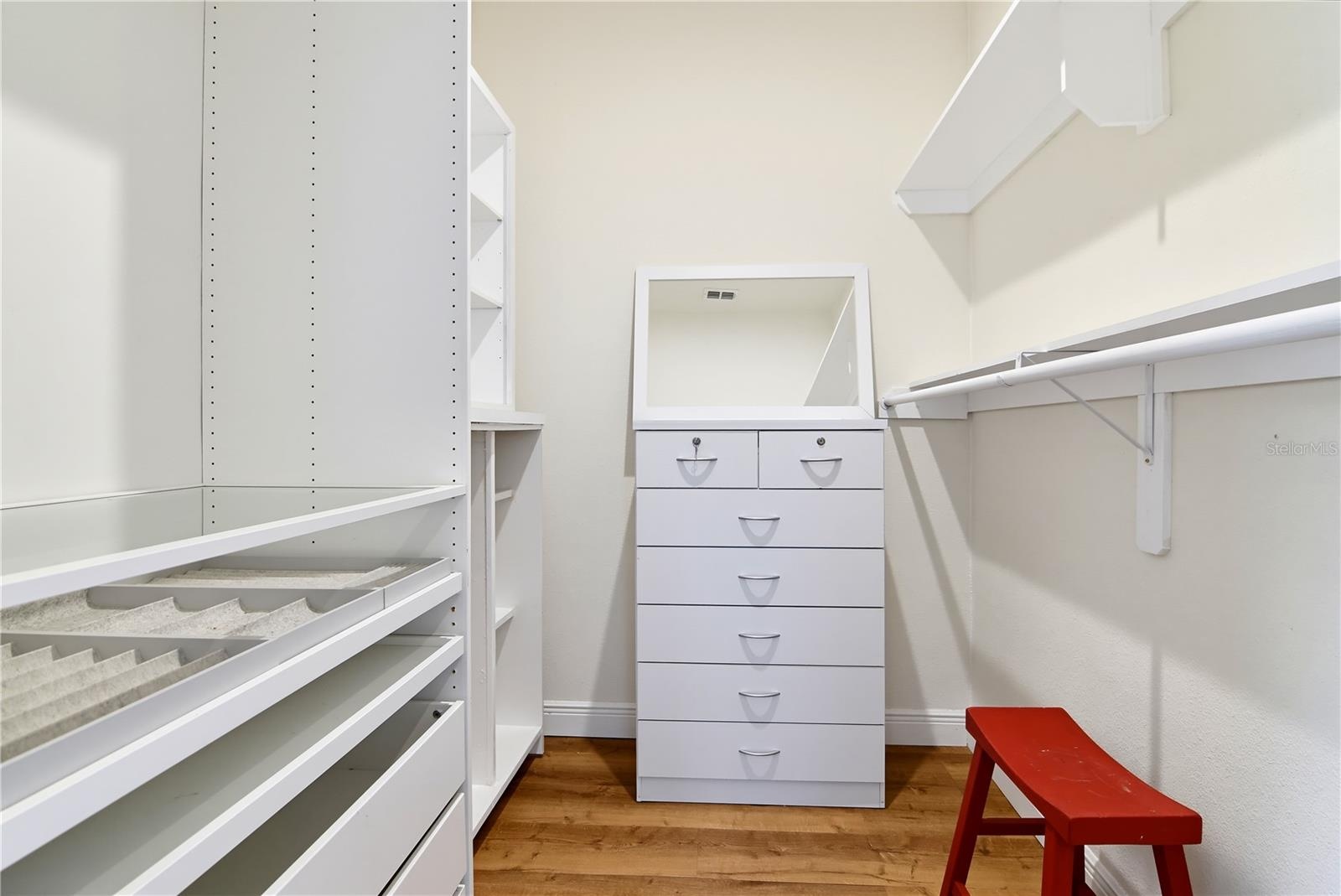 Walk-in primary closet with extensive built-in shelving, hanging space, and drawers.