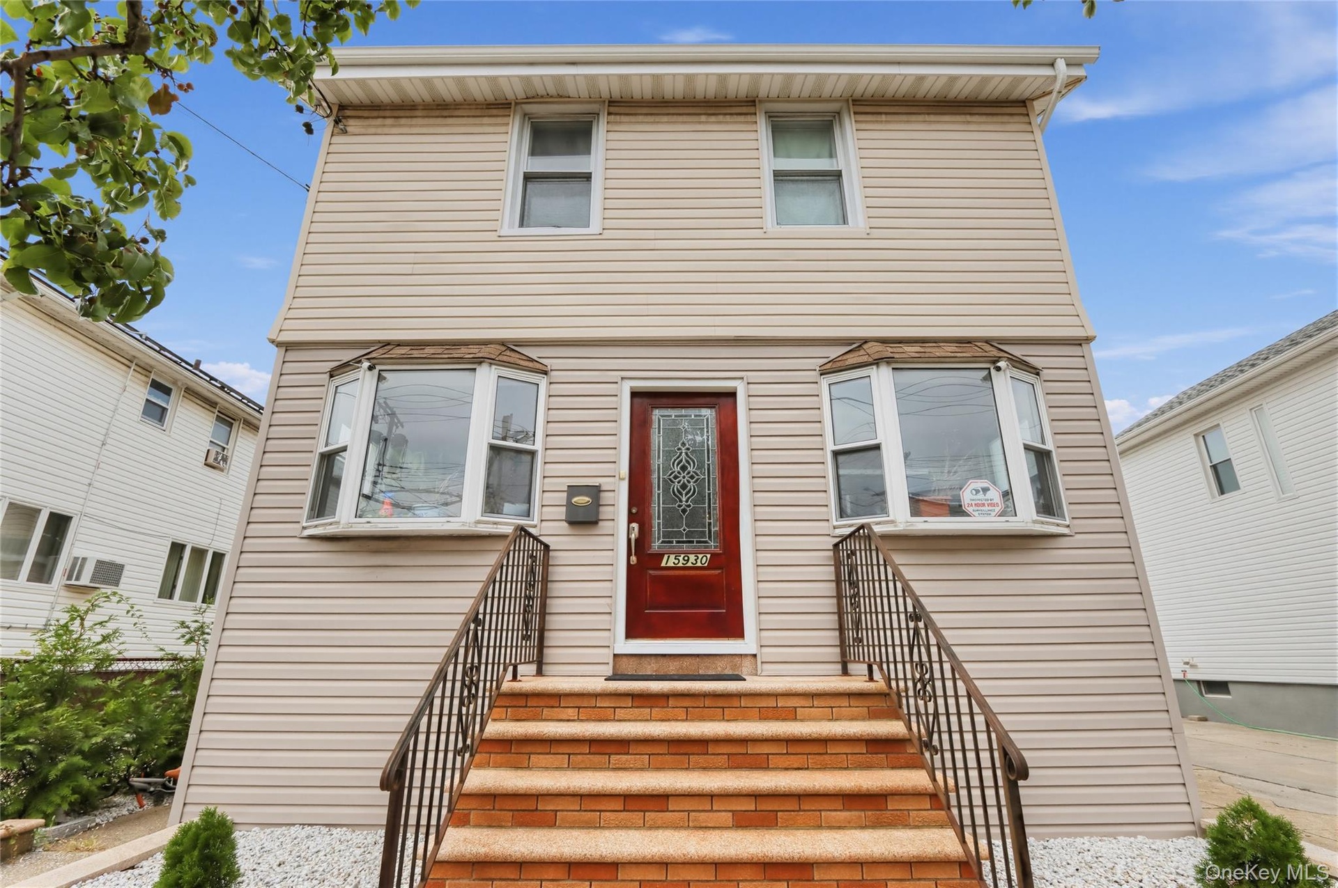Two-story residence featuring light-toned siding, a vibrant red entry door with decorative glass, and a bay window