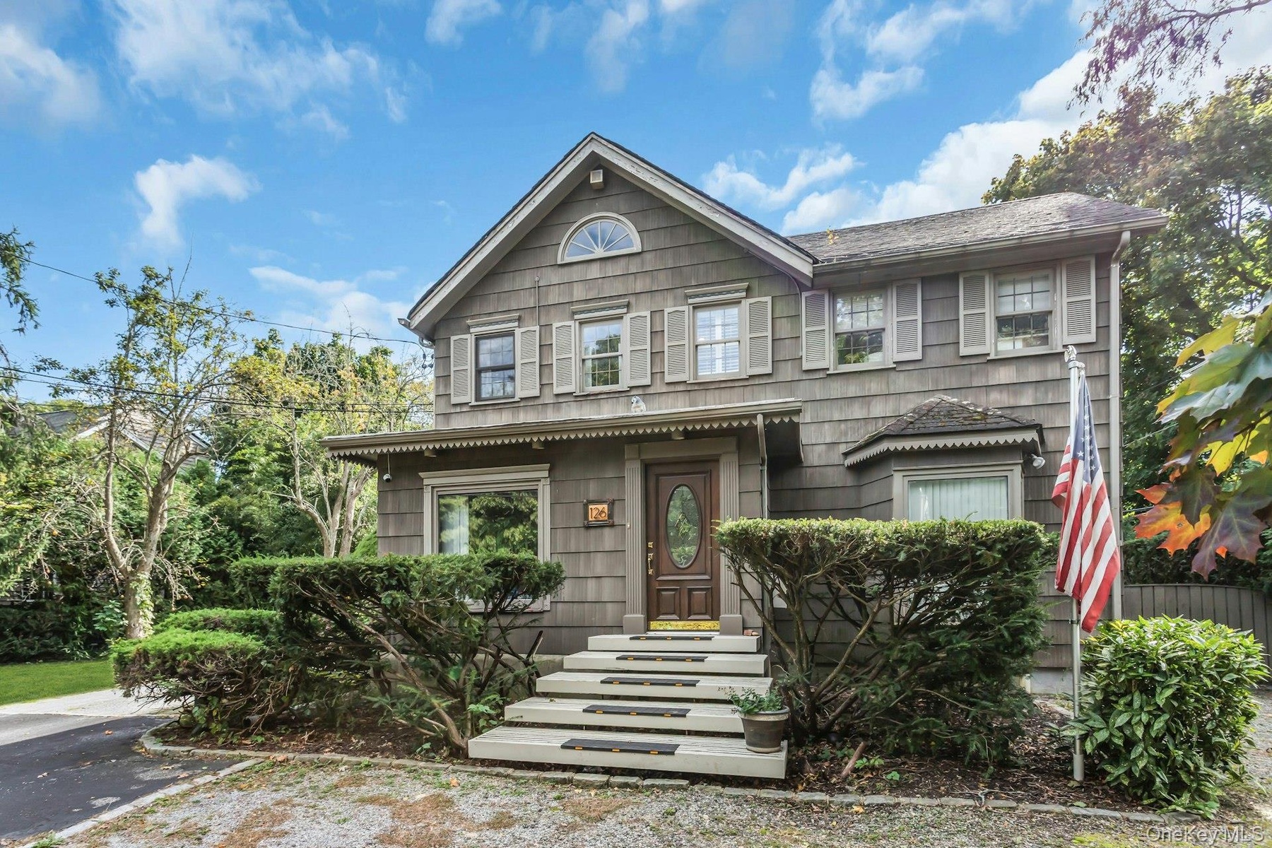 Shingle-sided exterior with a gabled roofline, decorative window shutters, a bay window, and a prominent front entrance with a paneled door
