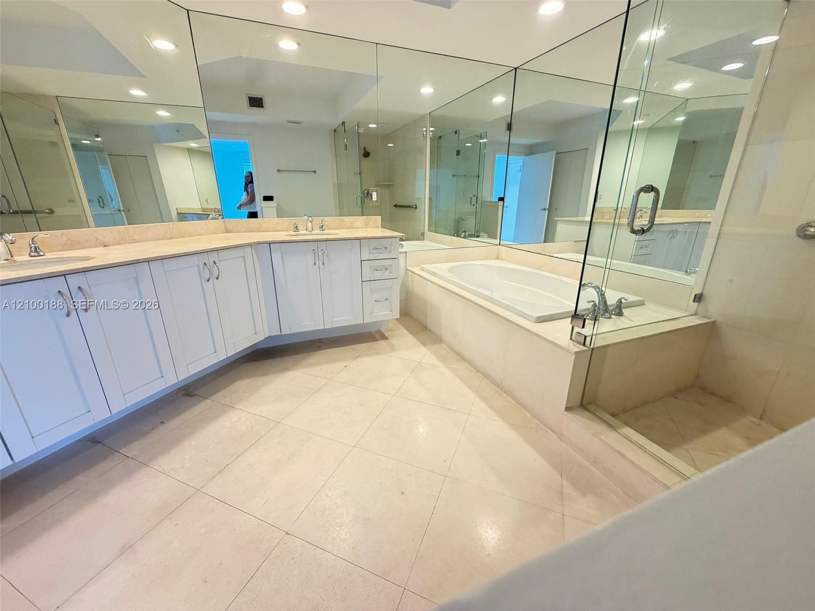 Bathroom featuring a double-sink vanity with white cabinetry and solid surface countertops, a built-in soaking tub, a glass-enclosed shower, expansive
