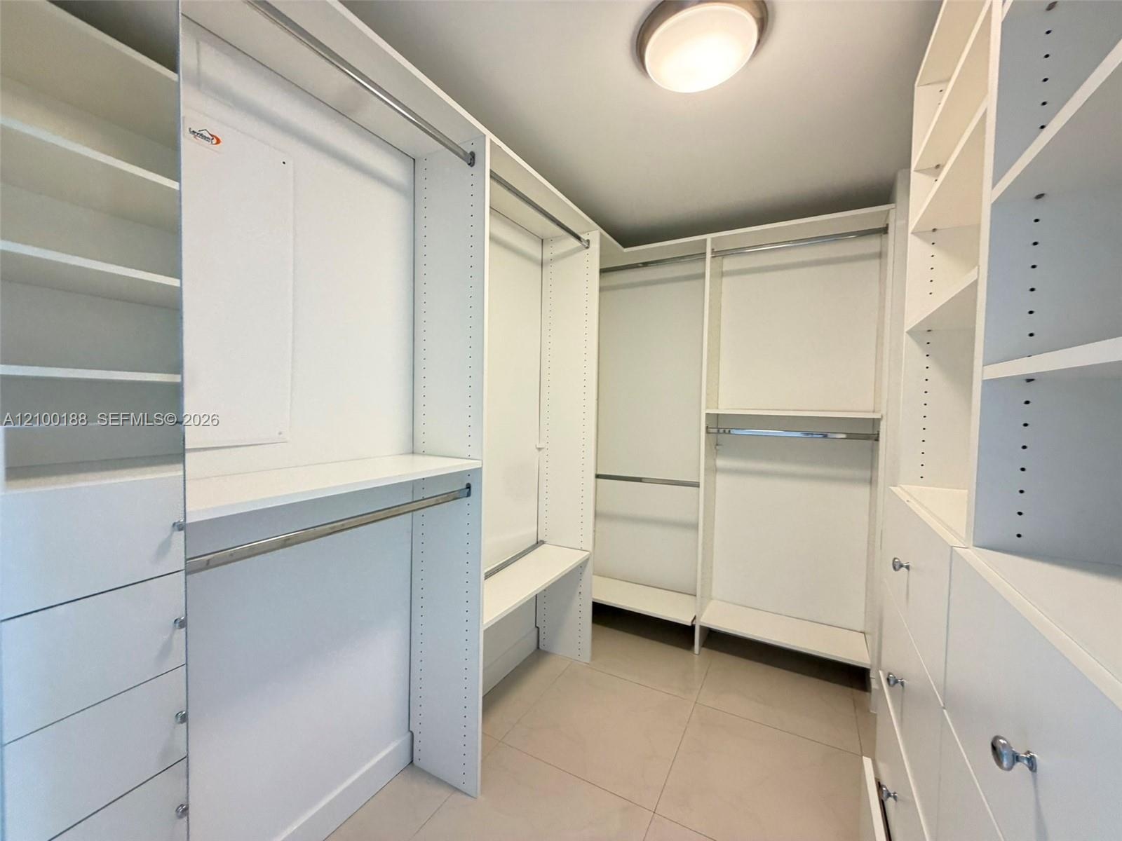 Walk-in closet featuring white custom built-in shelving, multiple hanging rods, integrated drawer storage, and tile flooring