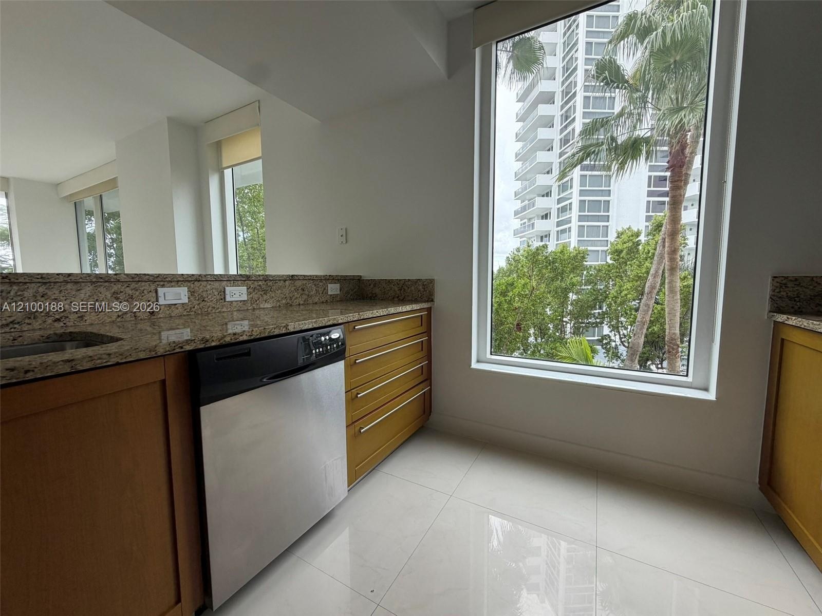 Kitchen featuring natural stone countertops, warm-toned wood cabinetry, stainless steel dishwasher, floor-to-ceiling windows, and polished tile floori
