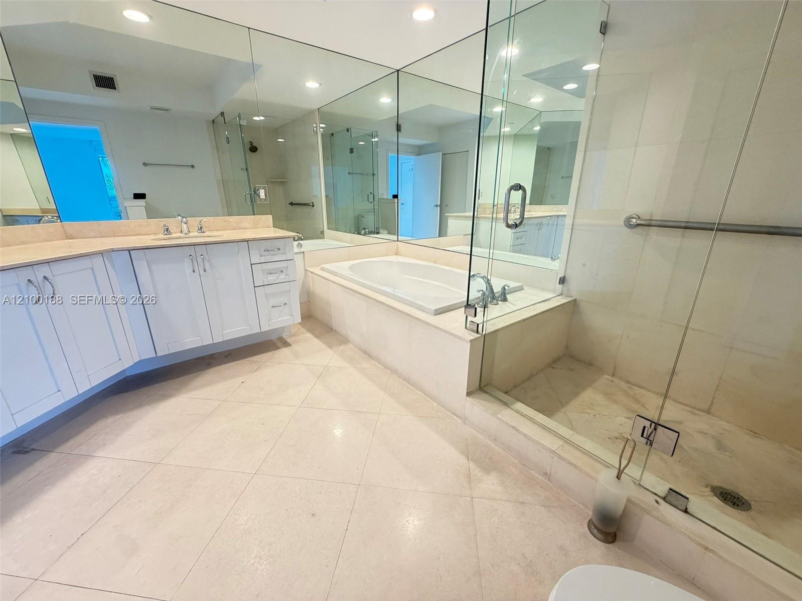 Bathroom featuring a double vanity with light-toned countertop, soaking tub with tile surround, glass-enclosed shower, expansive wall-to-wall mirrors,
