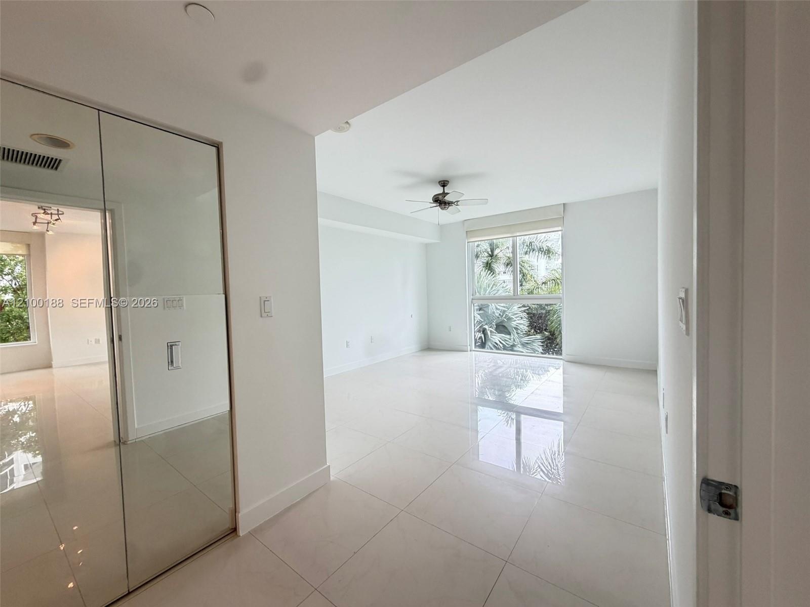 Large-format tile flooring, ceiling-mounted paddle fan, and floor-to-ceiling mirrored closet doors