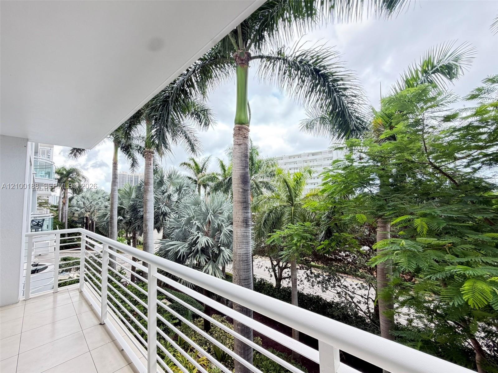 Private balcony featuring white horizontal railings, tile flooring, and mature palm trees