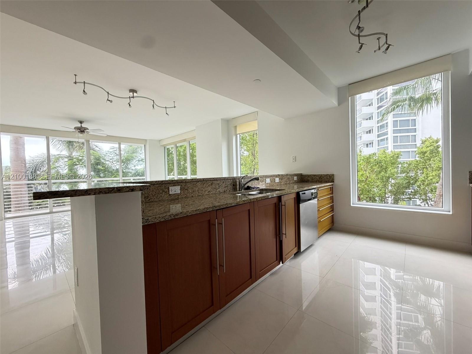Kitchen featuring stone countertops, wood cabinetry, stainless steel dishwasher, polished tile flooring, and floor-to-ceiling windows