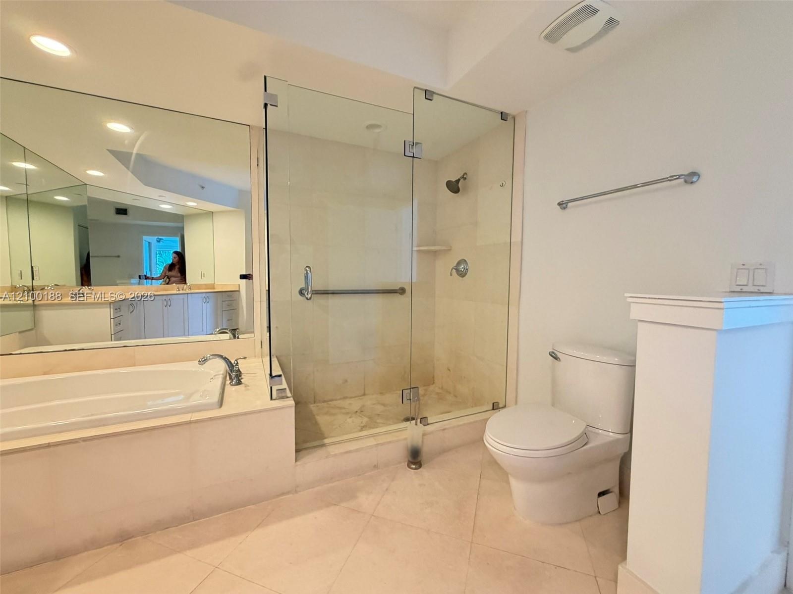 Bathroom featuring a soaking tub with a deck-mounted faucet, a frameless glass-enclosed shower, expansive wall-mounted mirror, and tile flooring