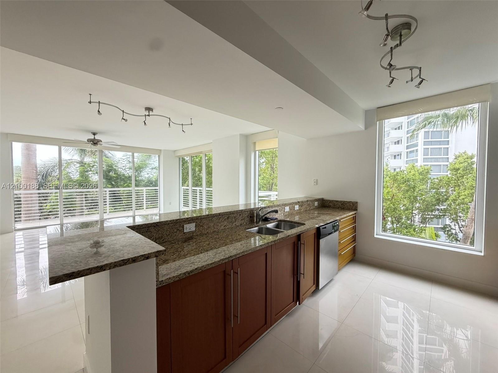 Kitchen featuring stone countertops, wood-finish cabinetry, stainless steel dishwasher, tile flooring, and track lighting