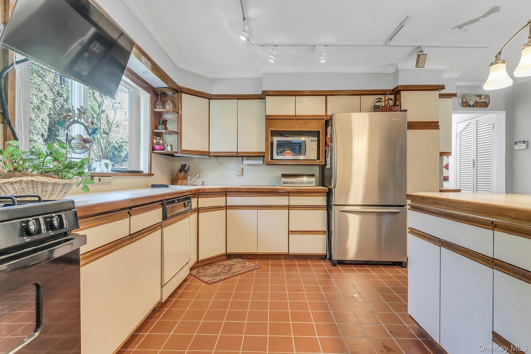 Kitchen featuring wood-finish countertops, extensive cabinetry with wood-trim details, stainless steel refrigerator, and terracotta tile flooring