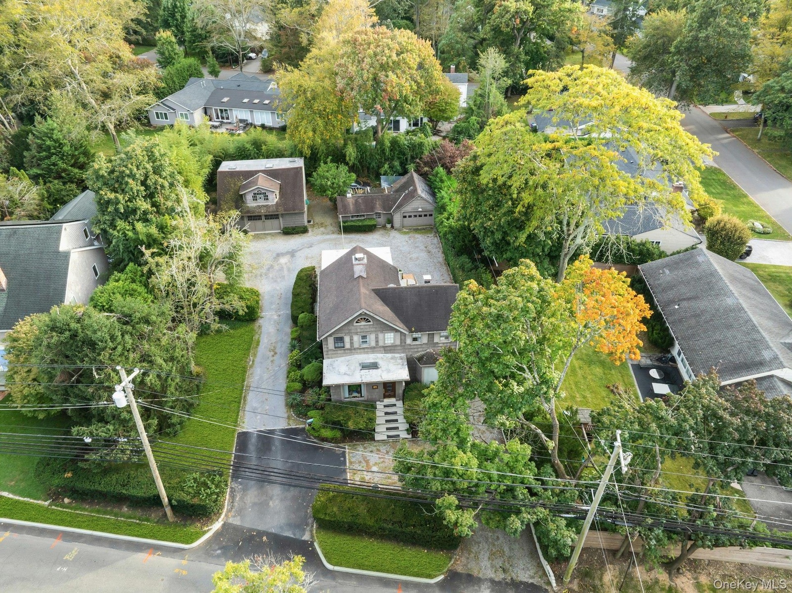 Shingle-sided residence with a dark-pitched roof, paved driveway, stone walkway, and established landscaping