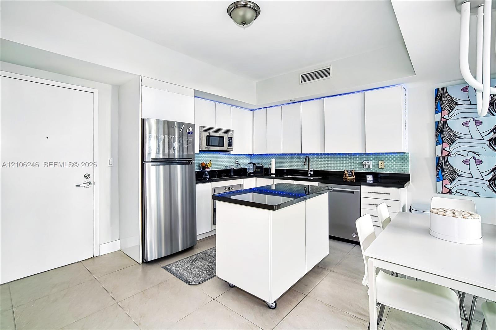 Kitchen featuring white flat-panel cabinetry, dark stone countertops, stainless steel appliances, a mobile center island, and tiled backsplash