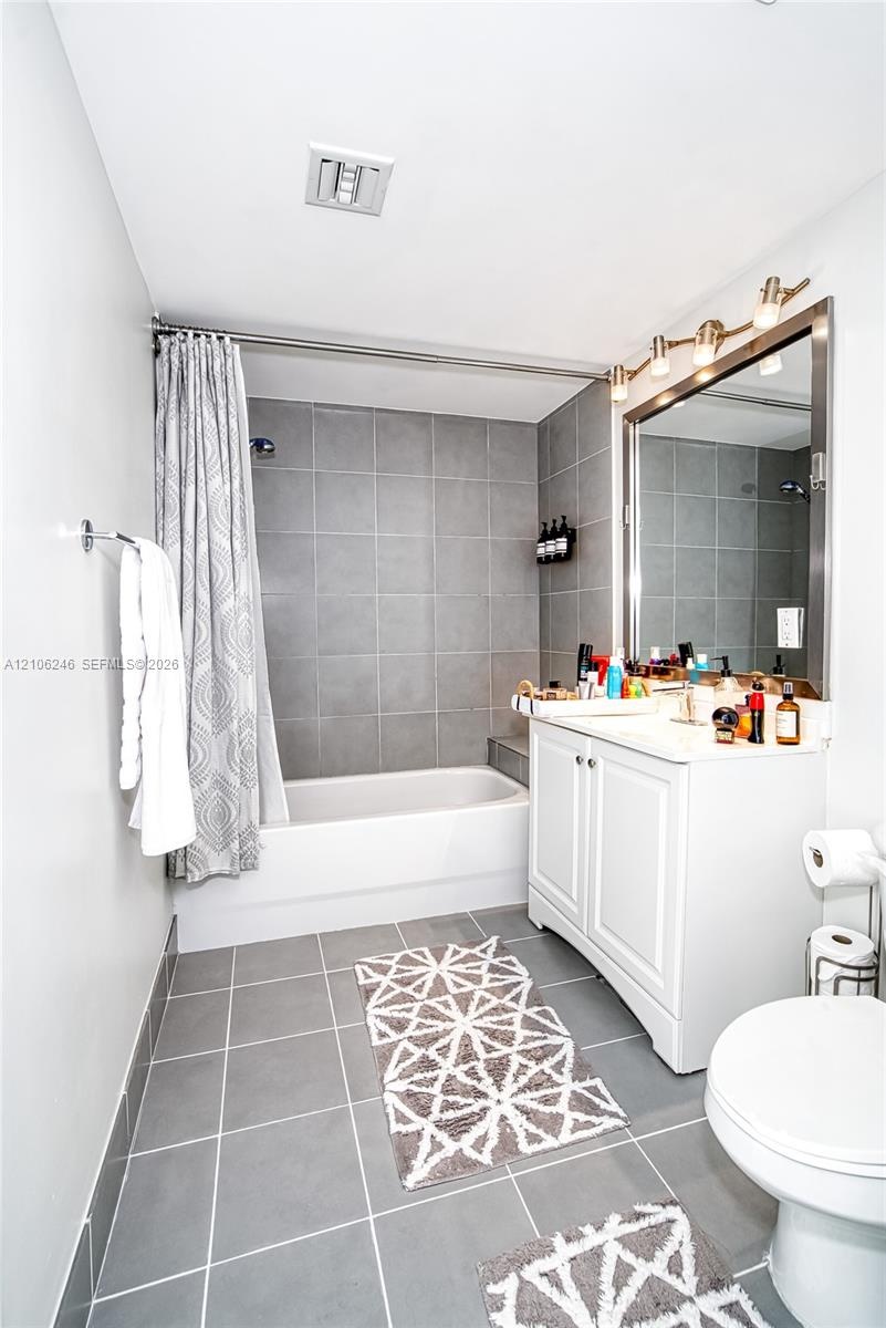 Bathroom featuring a white vanity cabinet, a rectangular mirror with a metal frame, a multi-bulb vanity light fixture, and a bathtub with gray tile su