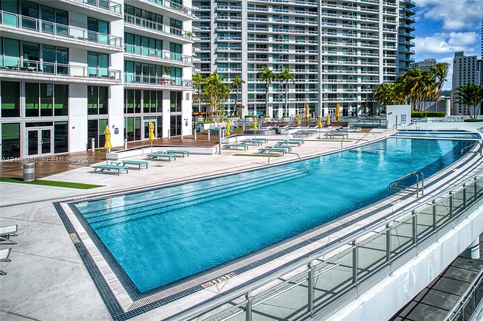 Expansive swimming pool with integrated stair entry, surrounded by a paved sun deck and wood-finish decking