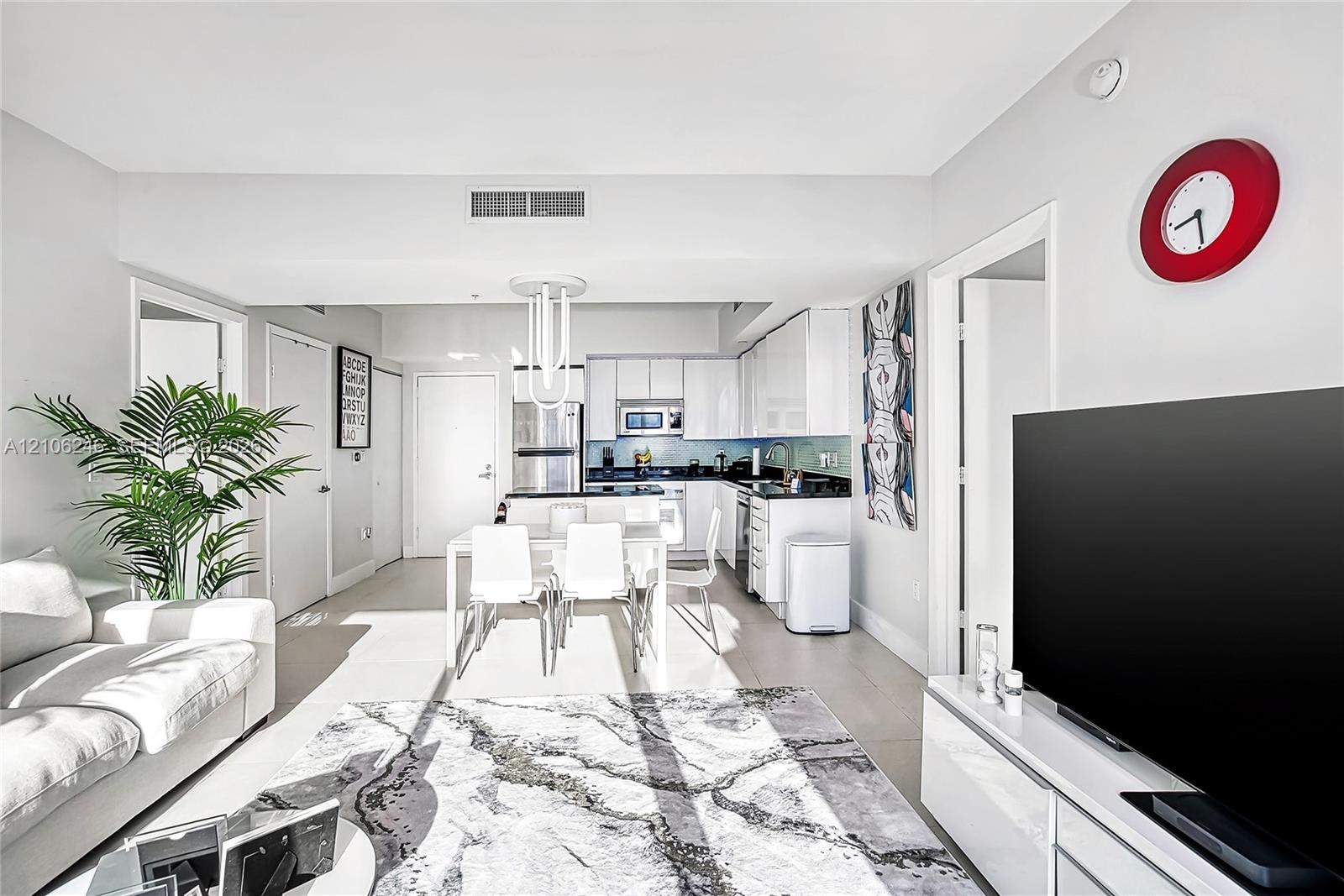 Open-concept kitchen featuring high-gloss cabinetry, stone countertops, stainless steel appliances, and a central peninsula