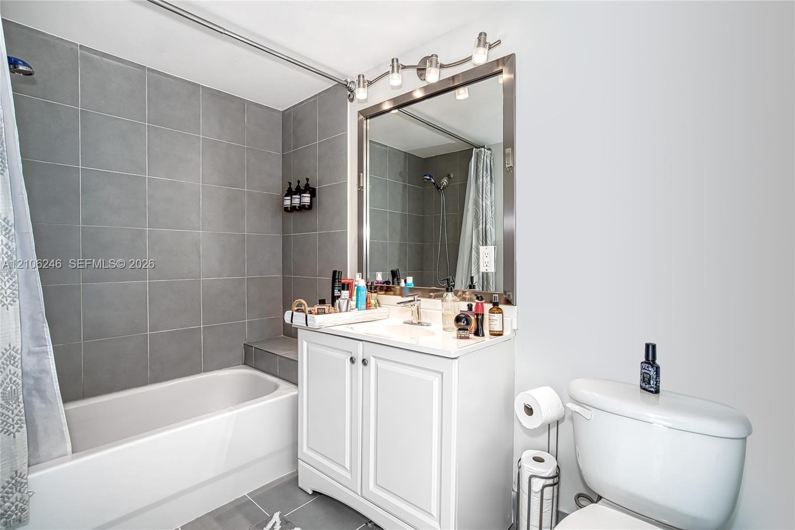 Bathroom featuring a white vanity with built-in cabinetry, a rectangular basin with a single-handle faucet, a framed mirror, a multi-bulb vanity light