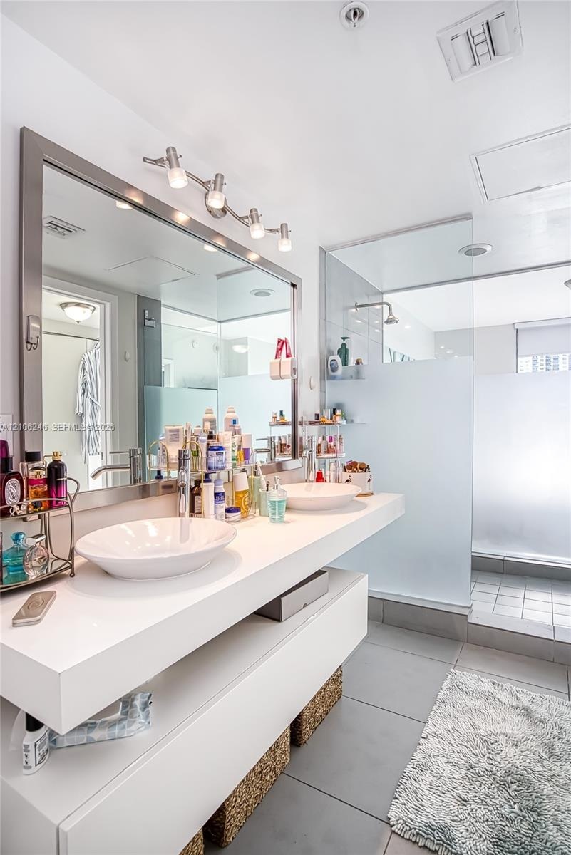 Floating white vanity with dual vessel sinks, large framed vanity mirror, and walk-in glass-enclosed shower with frosted privacy glass and oversized t