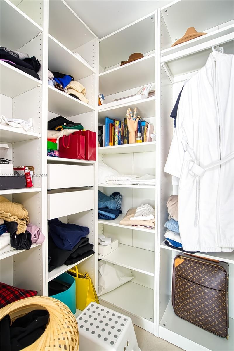 Custom walk-in closet featuring white floor-to-ceiling built-in cabinetry, adjustable open shelving, and integrated pull-out drawers