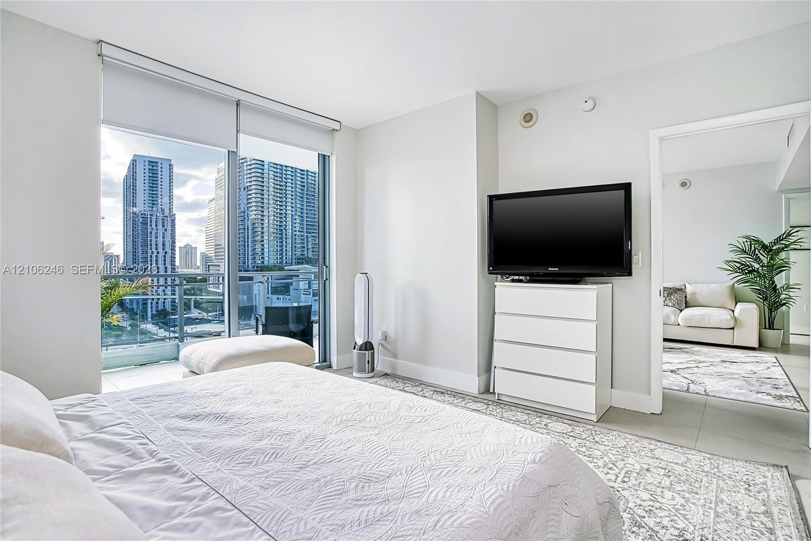Floor-to-ceiling glass sliding doors, private balcony, large-format tile flooring, and urban skyscraper backdrop