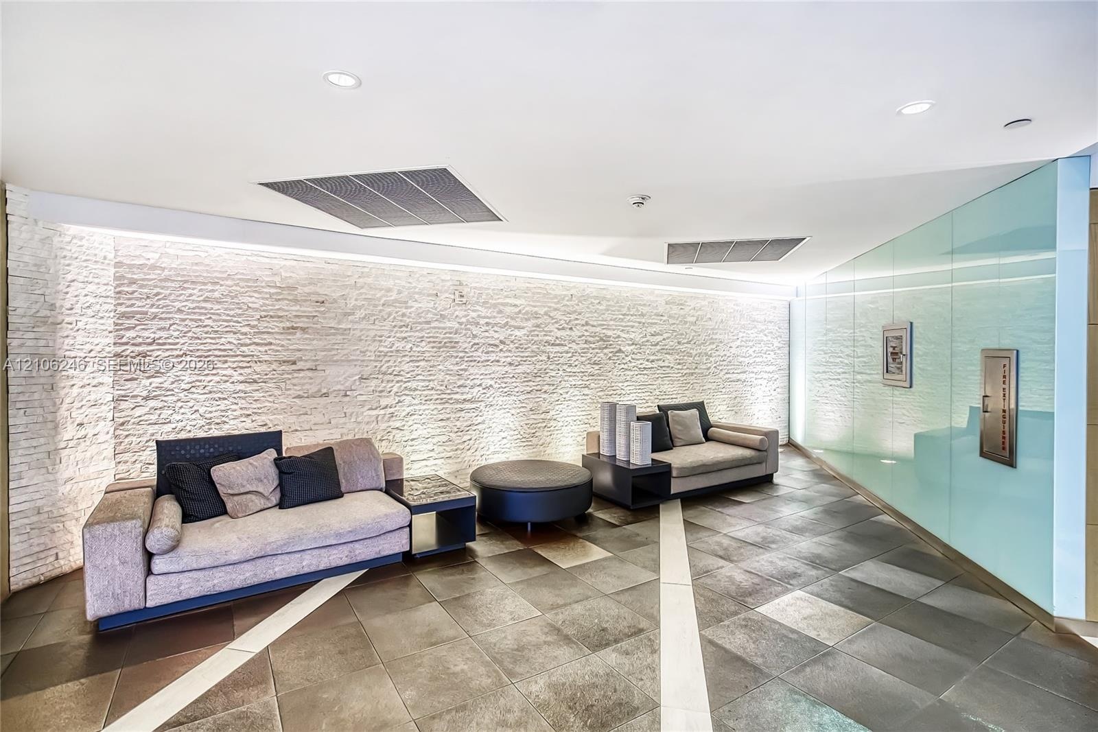 Curved stone-textured accent wall with integrated LED uplighting, large-format tile flooring with contrasting linear inlays, and floor-to-ceiling glas