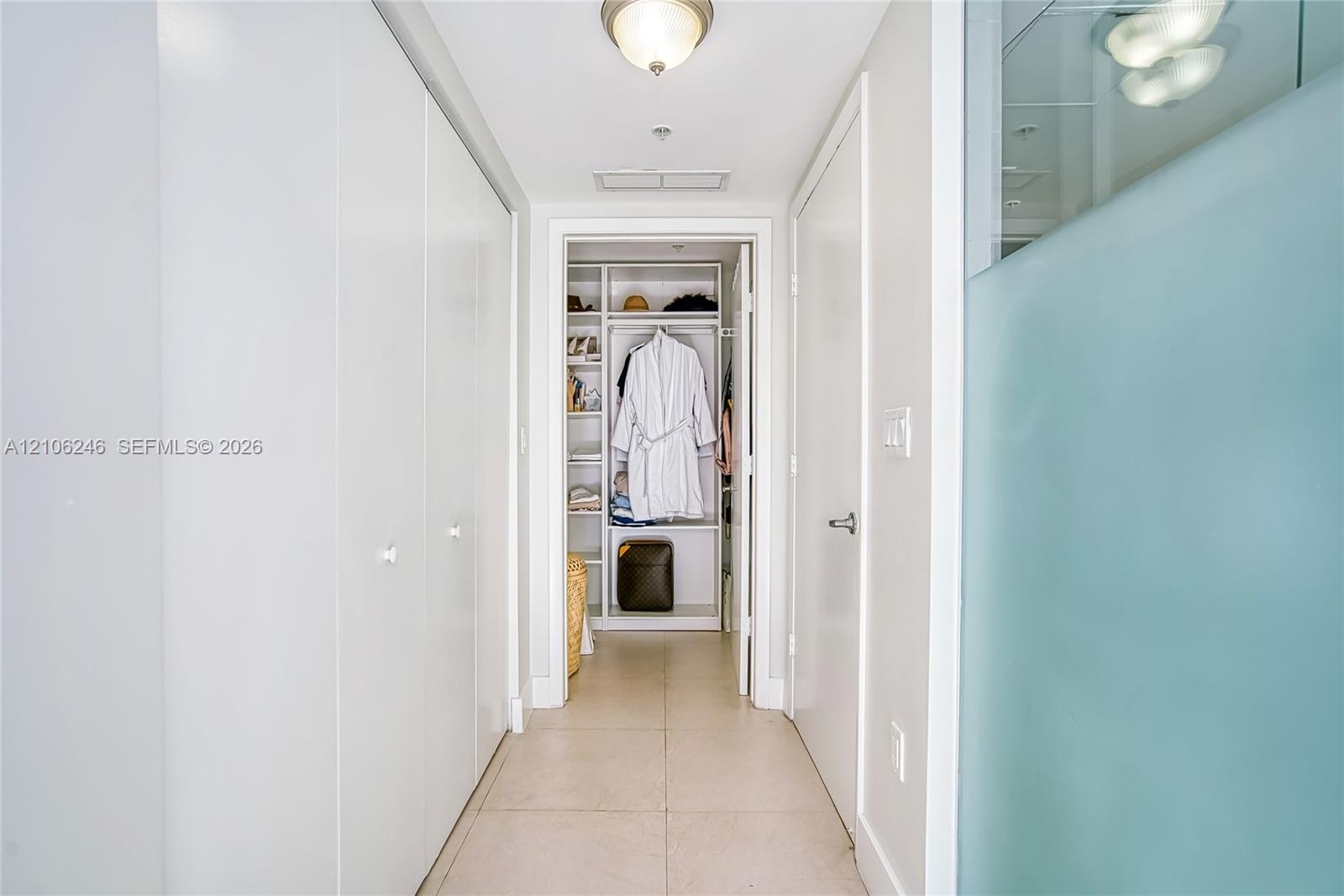 Hallway featuring large-format tile flooring, ceiling-mounted light fixtures, extensive floor-to-ceiling built-in cabinetry, and a walk-in closet with